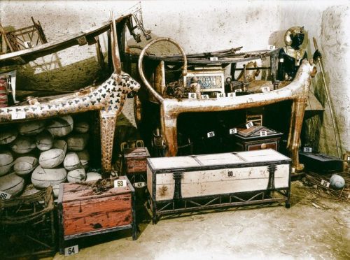 دسامبر ۱۹۲۲ میلادی/ مقبره توت عنخ آمون /  جعبه سفید مستطیل شکل که در جلوی کاناپه شیر قرار دارد، شامل لباس‌های کتان، ۶۹ تیر و یک شیپور است